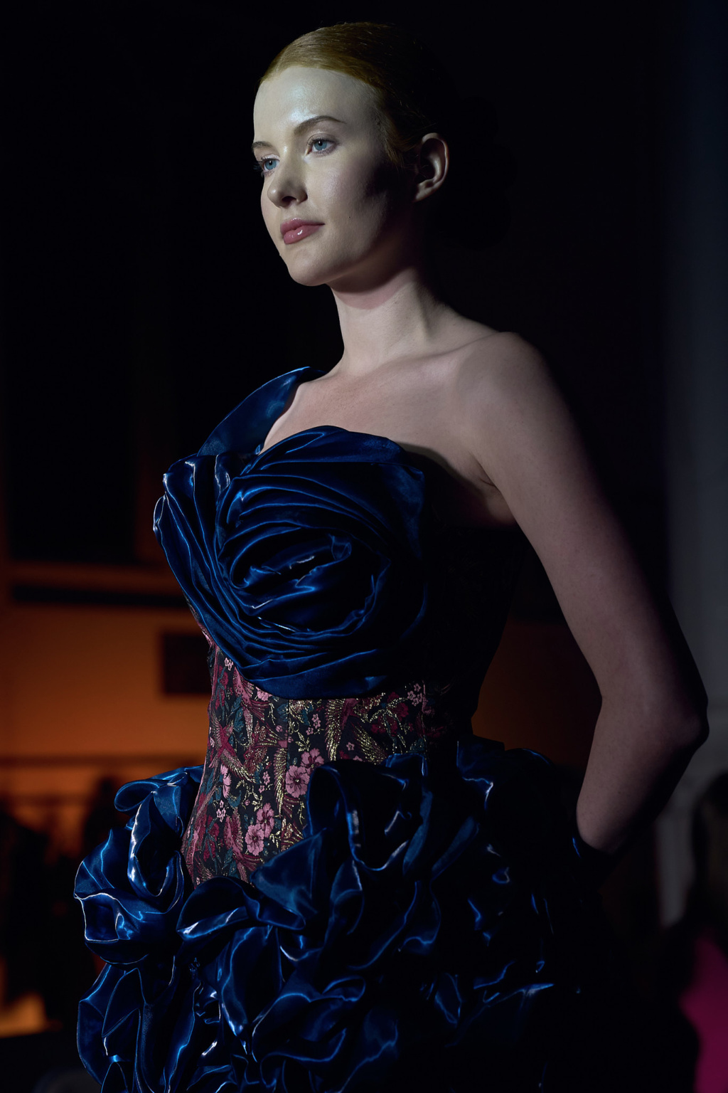 Fashion portrait, model wearing sculptural royal blue satin gown with floral brocade corset, dramatic low lighting