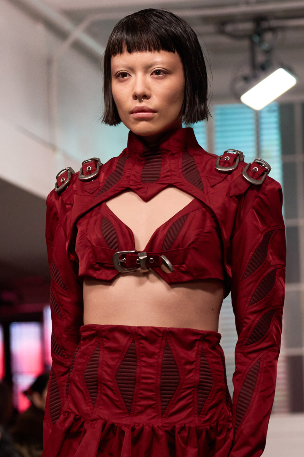 Fashion Portrait, model wearing sculptural crimson co-ord set with cutout panels and silver buckle hardware, runway lighting