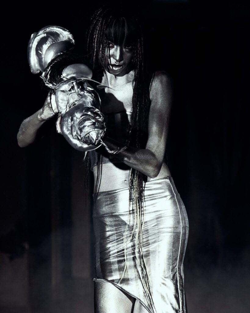 Fashion show, LFW AW26 Silvercity, model wearing a silver skirt, dark moody lighting