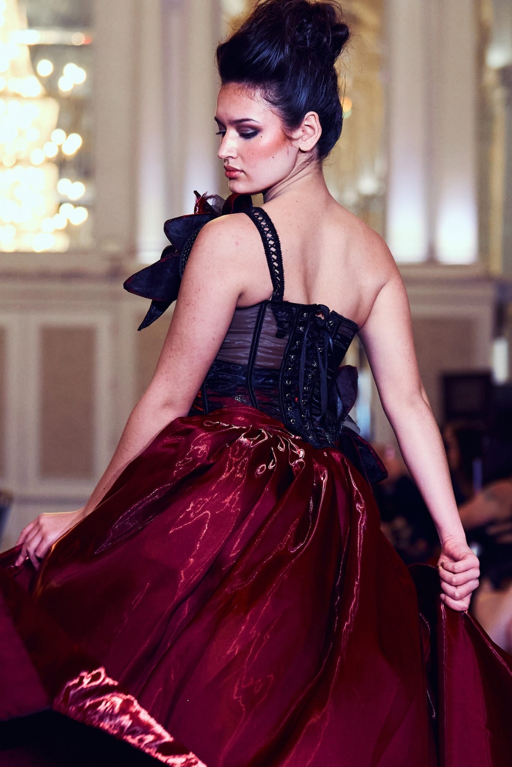 Fashion portrait, model in red gown and black corset decorate with flower pieces, runway lighting
