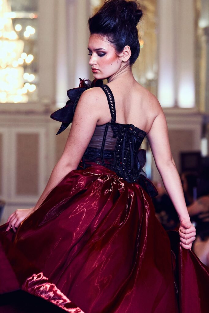 Fashion portrait, model in red gown and black corset decorate with flower pieces, runway lighting