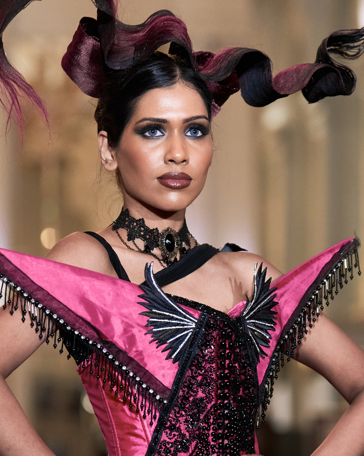 Fashion portrait, model in sculptural fuchsia and black beaded corset with dramatic horned headpiece, runway lighting