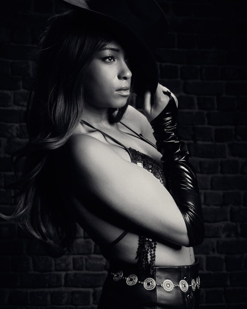 Fashion portrait, Sin City inspired, model wearing hat, vinyl gloves and leather trousers with silver belt, dramatic chiaroscuro high contrast lighting