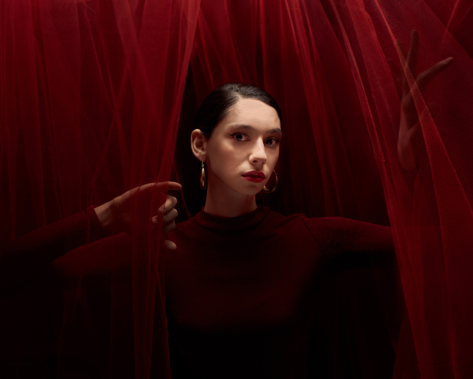 Editorial portrait, model in deep red dress surrounded by red veil fabric, moody cinematic lighting