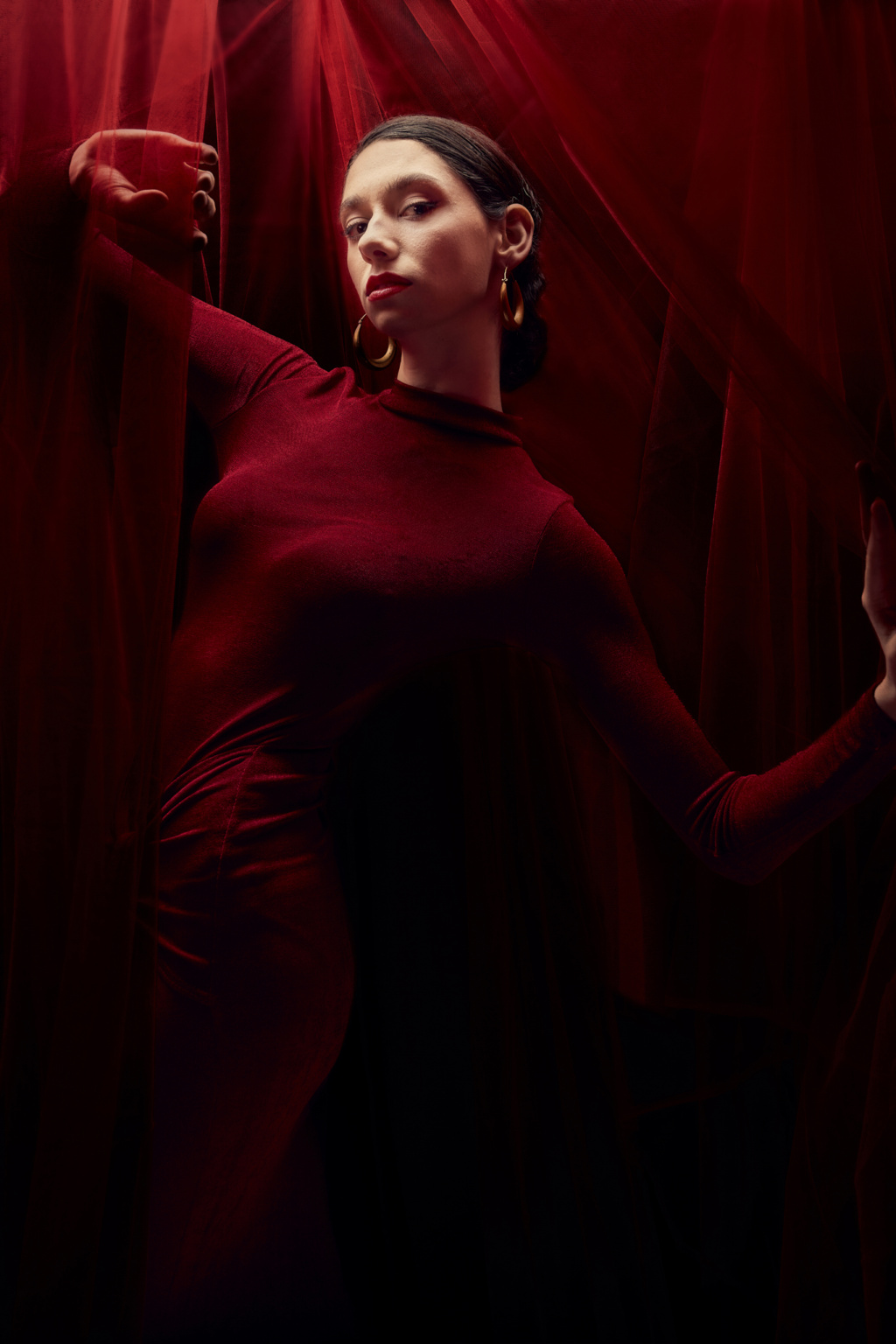 Editorial portrait, model in deep red long bodycon dress with drape detail, surrounded by red veil fabric, moody cinematic lighting