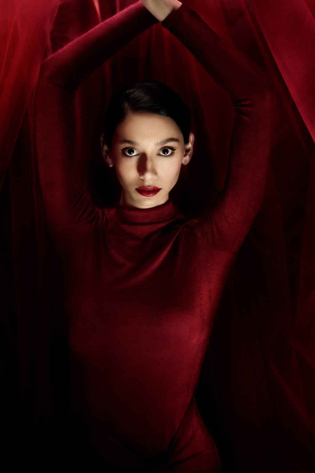 Editorial portrait, model in deep red dress surrounded by red draping fabric, moody atmospheric lighting